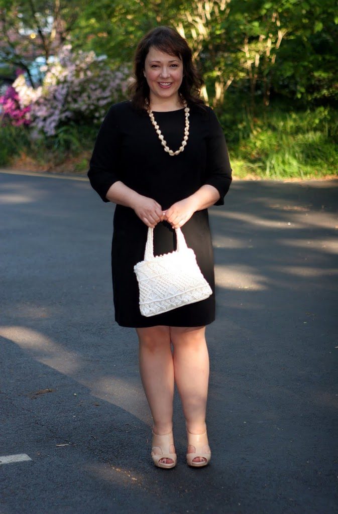 Alison Gary of Wardrobe Oxygen in a black bracelet sleeve sheath dress holding a white crocheted vintage handbag