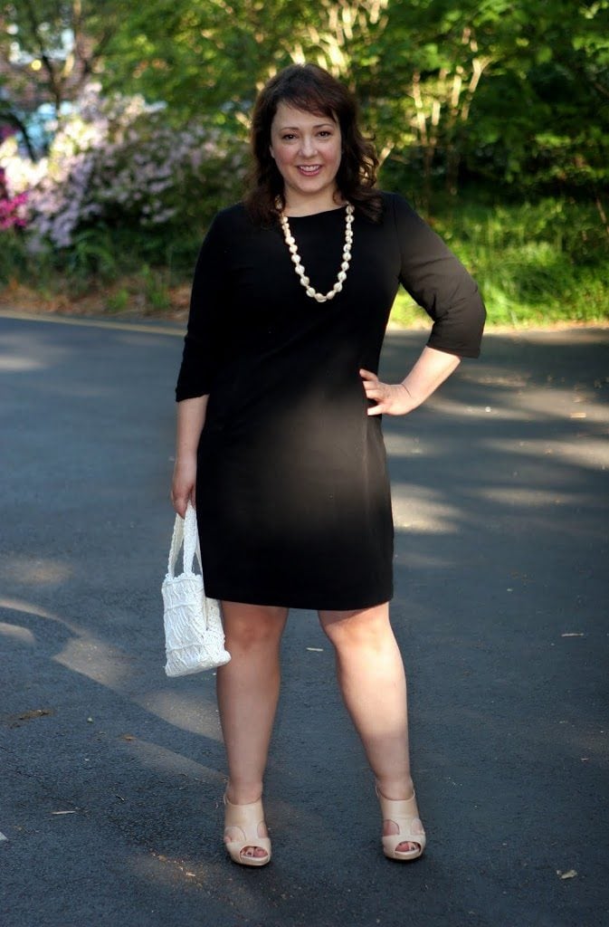 Alison Gary of Wardrobe Oxygen in a black bracelet sleeve sheath dress holding a white crocheted vintage handbag