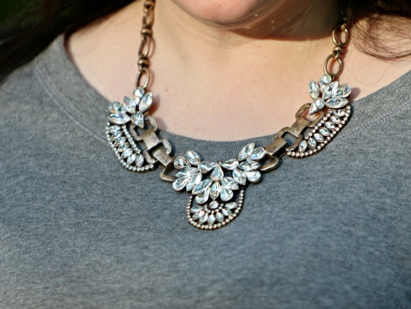 closeup of a crystal and gold statement necklace worn with a gray sweatshirt