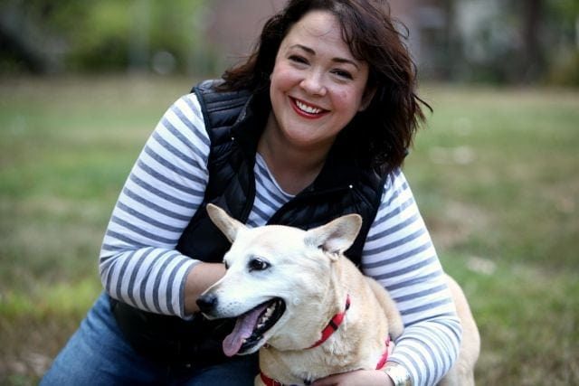 woman hugging a blonde dog, smiling at the camera