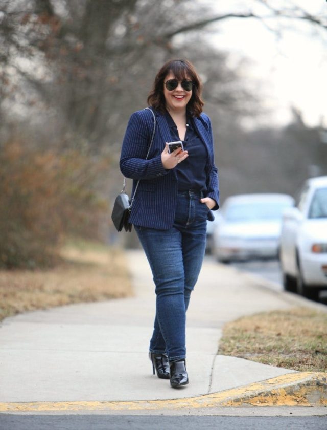 Alison Gary of Wardrobe Oxygen walking down a city street wearing a navy pinstripe blazer from Banana Republic with Universal Standard Seine jeans and black patent ankle booties