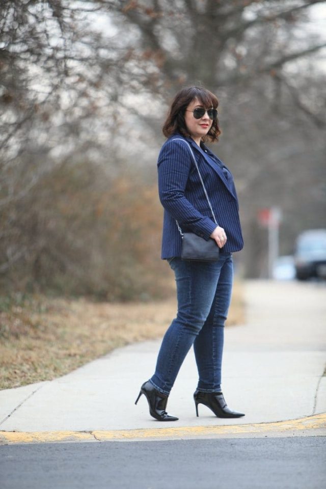 Alison Gary of Wardrobe Oxygen walking down a city street wearing a navy pinstripe blazer from Banana Republic with Universal Standard Seine jeans and black patent ankle booties