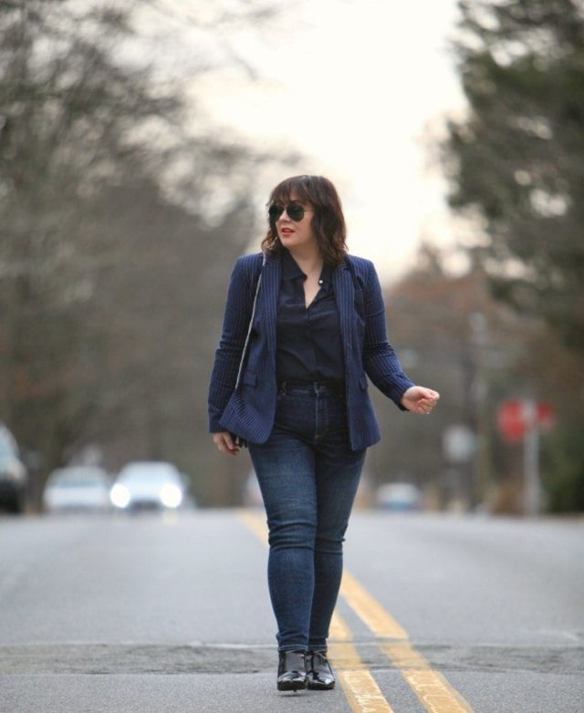 Alison Gary of Wardrobe Oxygen walking down a city street wearing a navy pinstripe blazer from Banana Republic with Universal Standard Seine jeans and black patent ankle booties