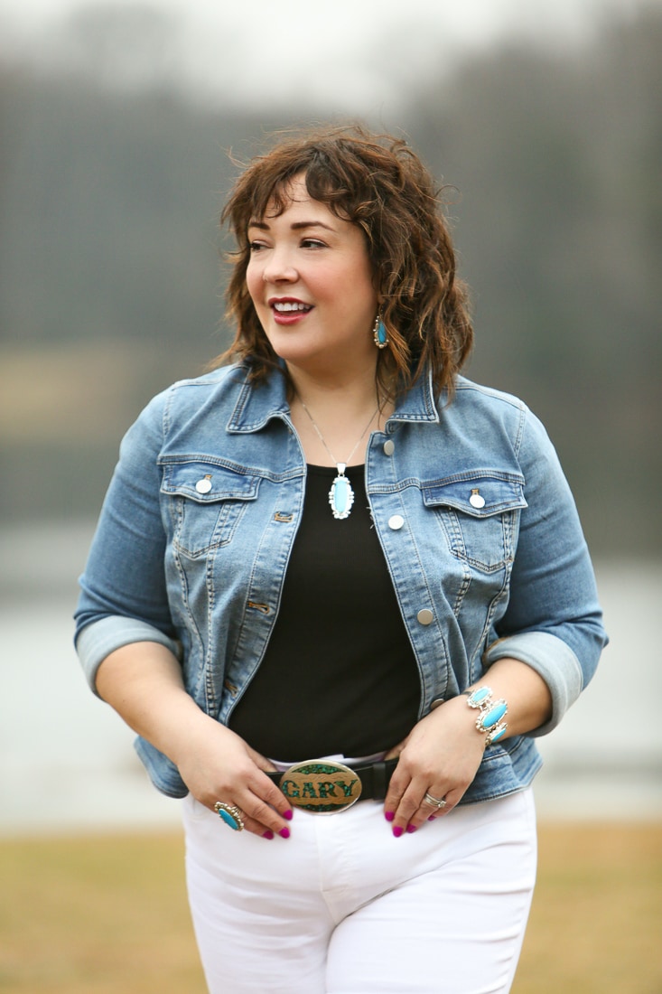 Alison in a denim jacket, black tank, and white jeans with a black leather belt and a silver buckle that says Gary in turquoise