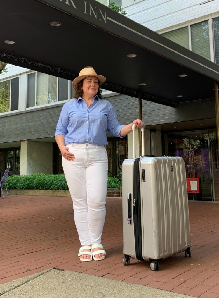 Alison Gary of Wardrobe Oxygen in front of a hotel in Georgetown, standing next to a large Delsey Helium rolling suitcase