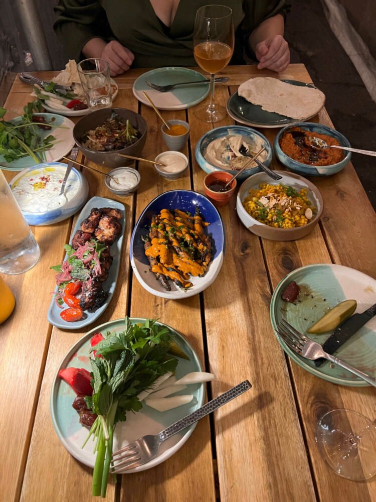 a wood dining table covered with plates of varying sizes with different middle eastern and mediterranean foods on them.