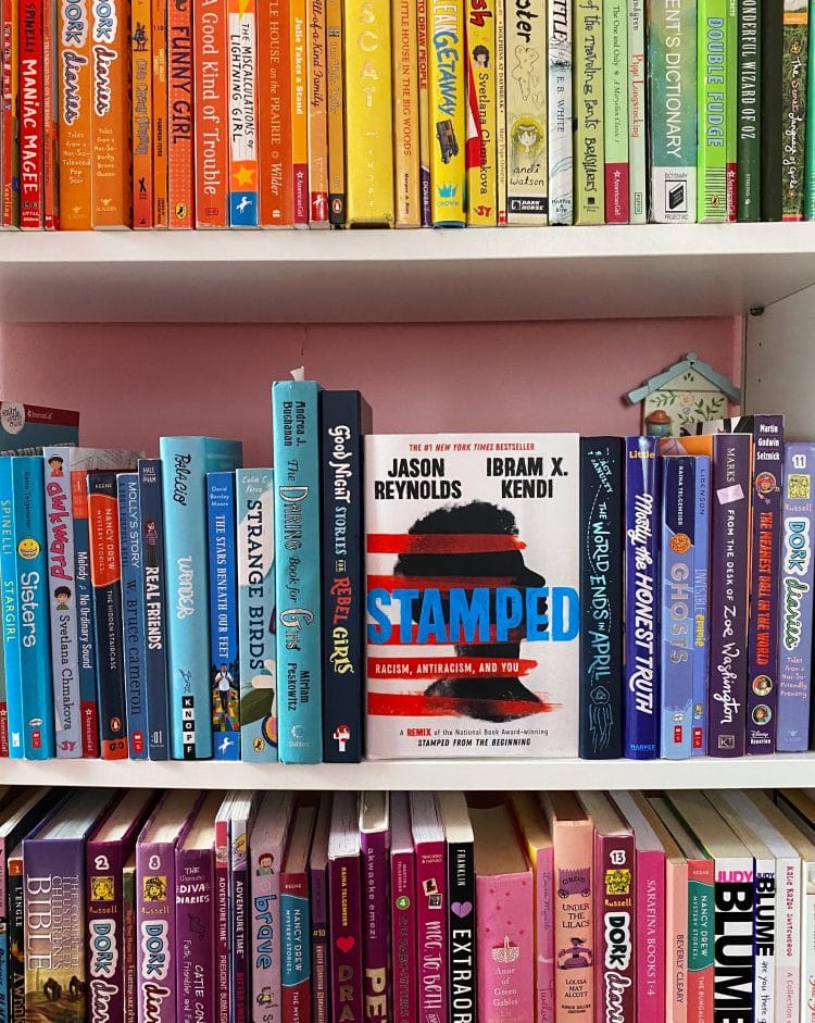 a bookcase full of colorful books for tweens and teens. In the middle is the book Stamped by Jason Reynolds and Ibram X. Kendi