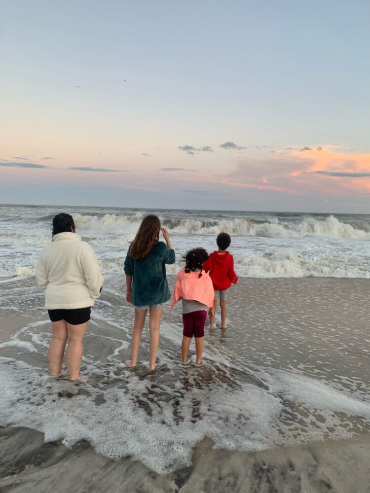 Three children and an adult standing in the waves at Davis Park, Fire Island, at sunset