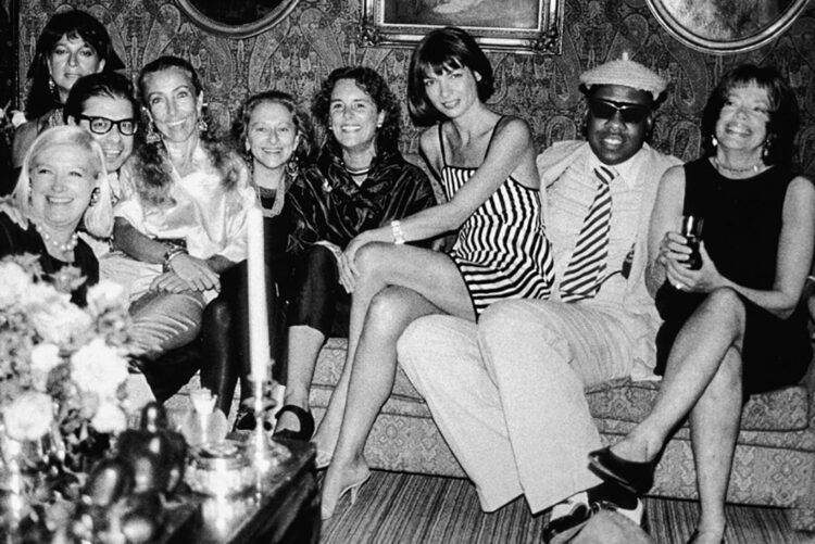 A group shot of fashionable people including Andre Leon Talley and Anna Wintour sitting on his lap