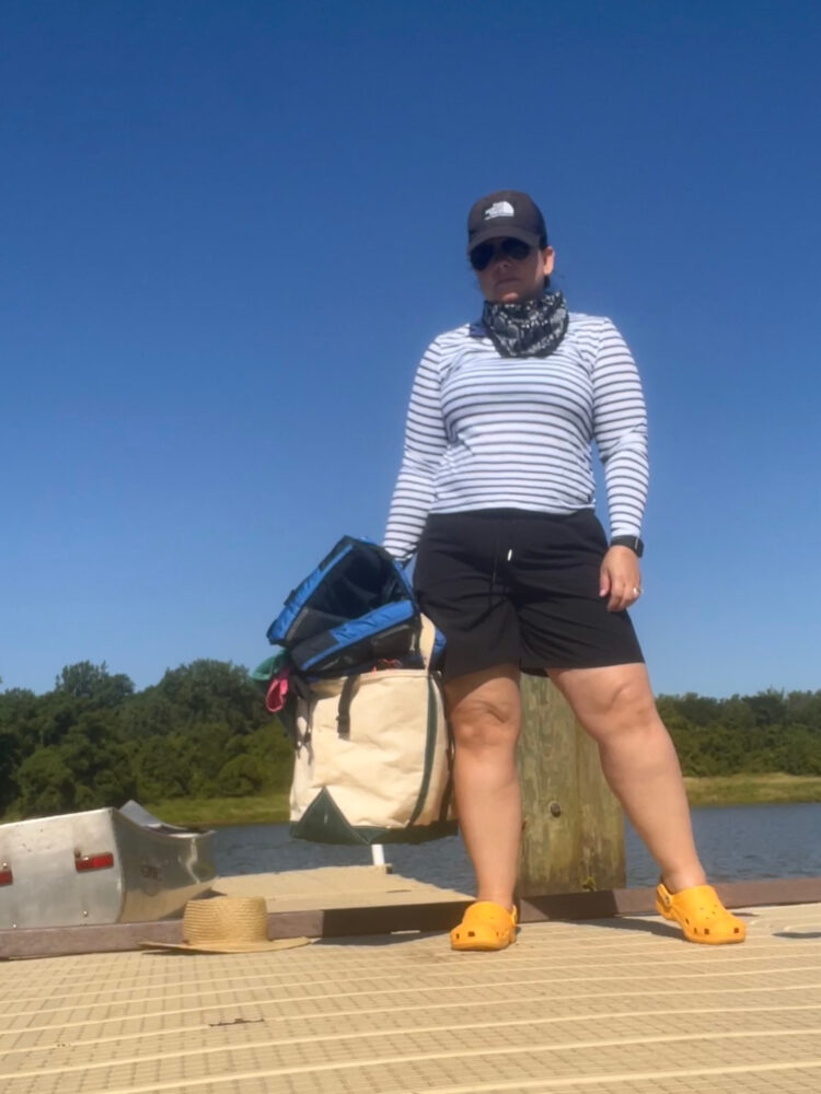 Alison Gary of Wardrobe Oxygen is standing on a dock on the Anacostia River. She is wearing a Lands' End striped rashguard and black Zenergy shorts from Chico's. She is holding a canvas tote and has Crocs on her feet.