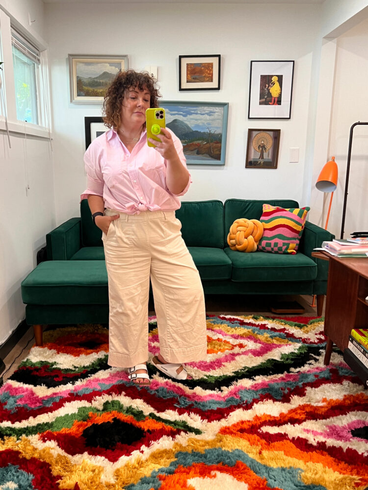 Alison Gary of Wardrobe Oxygen in her office at the Granite Building. She is wearing beige pull-on chino ankle pants and a pink button-front shirt tied at the waist.