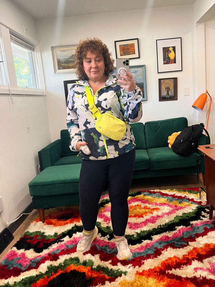 Alison in a navy print North Face windbreaker, navy leggings, and a highlighter yellow belt bag worn as a crossbody that she got at Lululemon