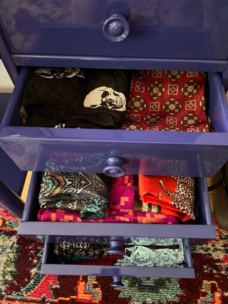 three drawers of a lacquered chest of drawers holding folded scarves
