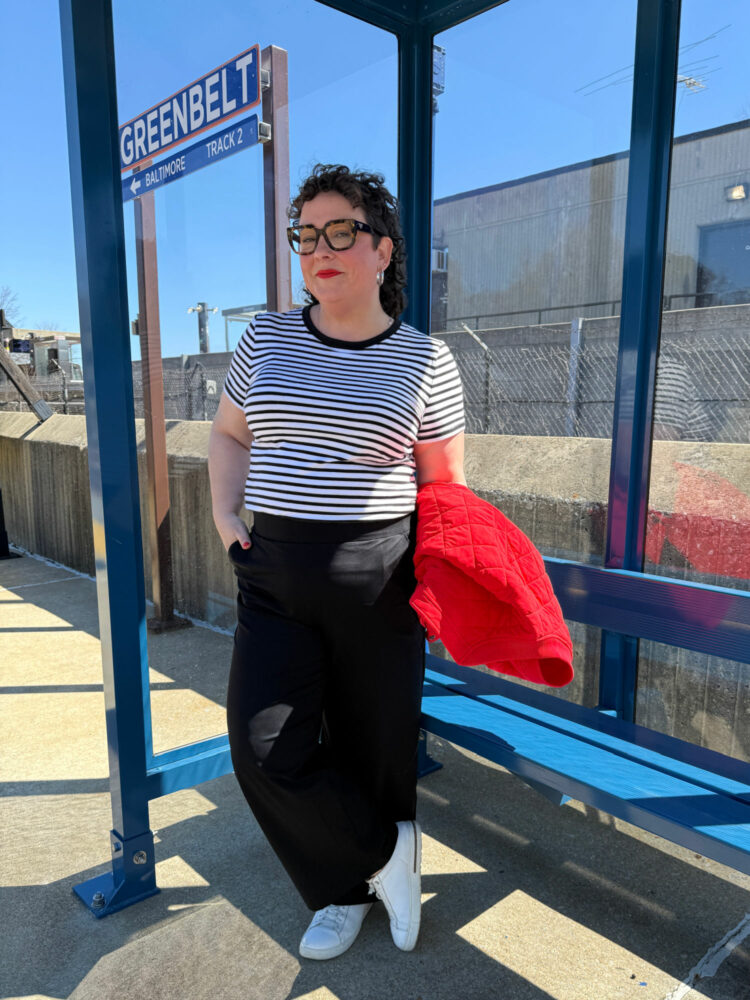 alison gary of wardrobe oxygen in a striped tee and black pants standing at a train station