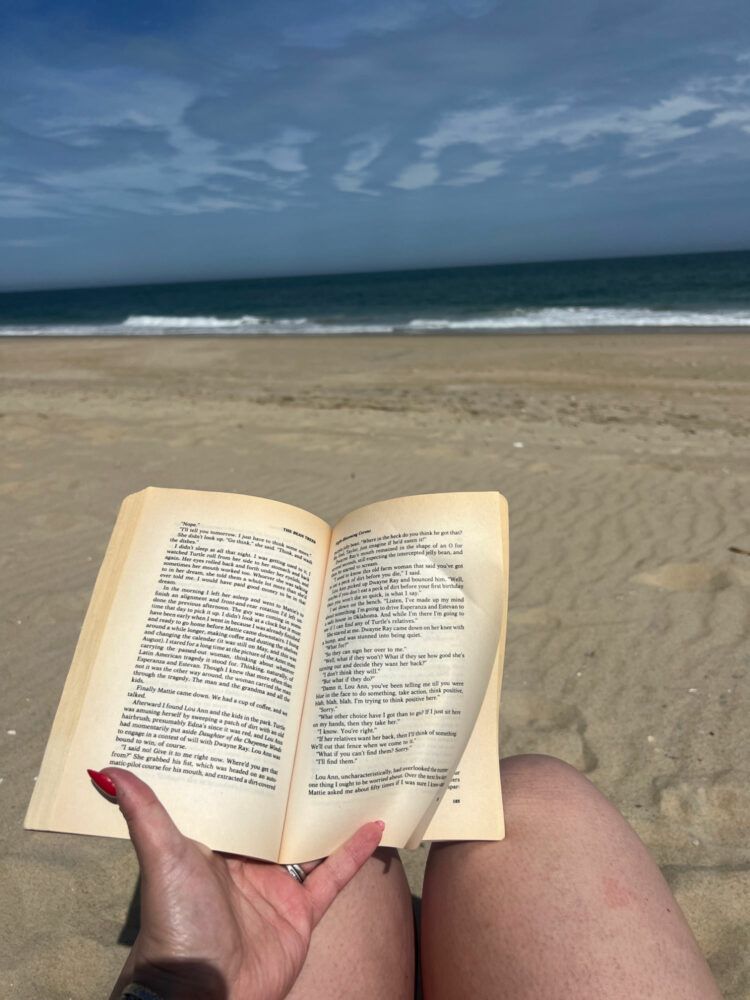 woman reading a book while sitting on the beach overlooking the atlantic ocean