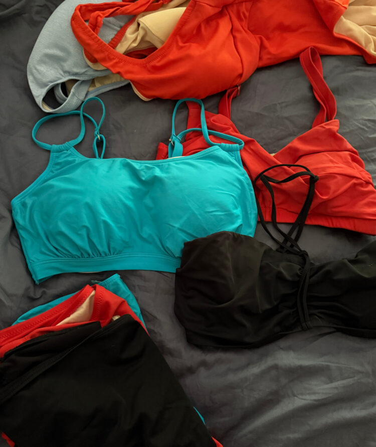 What Clothes I Pack Away on Labor Day - in photo:  two-piece and one-piece swimsuits in turquoise, blue, black, and orange lying on a bed